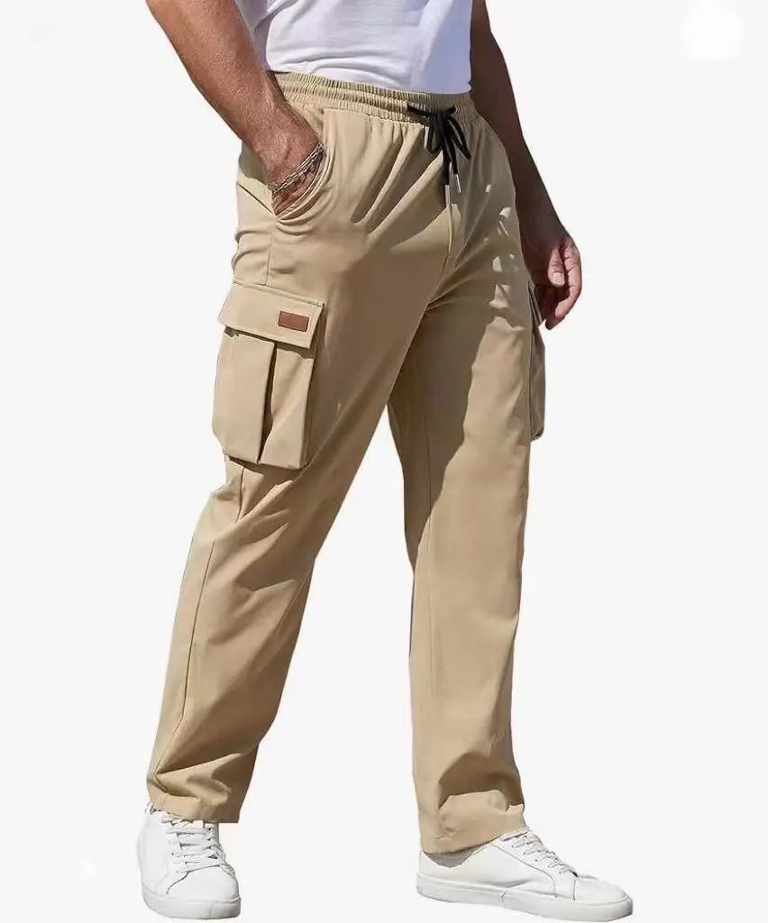 Man in beige cargo pants with loose fit, utility flap pockets, and drawstring waistband, styled with a white shirt and sneakers for casual wear.